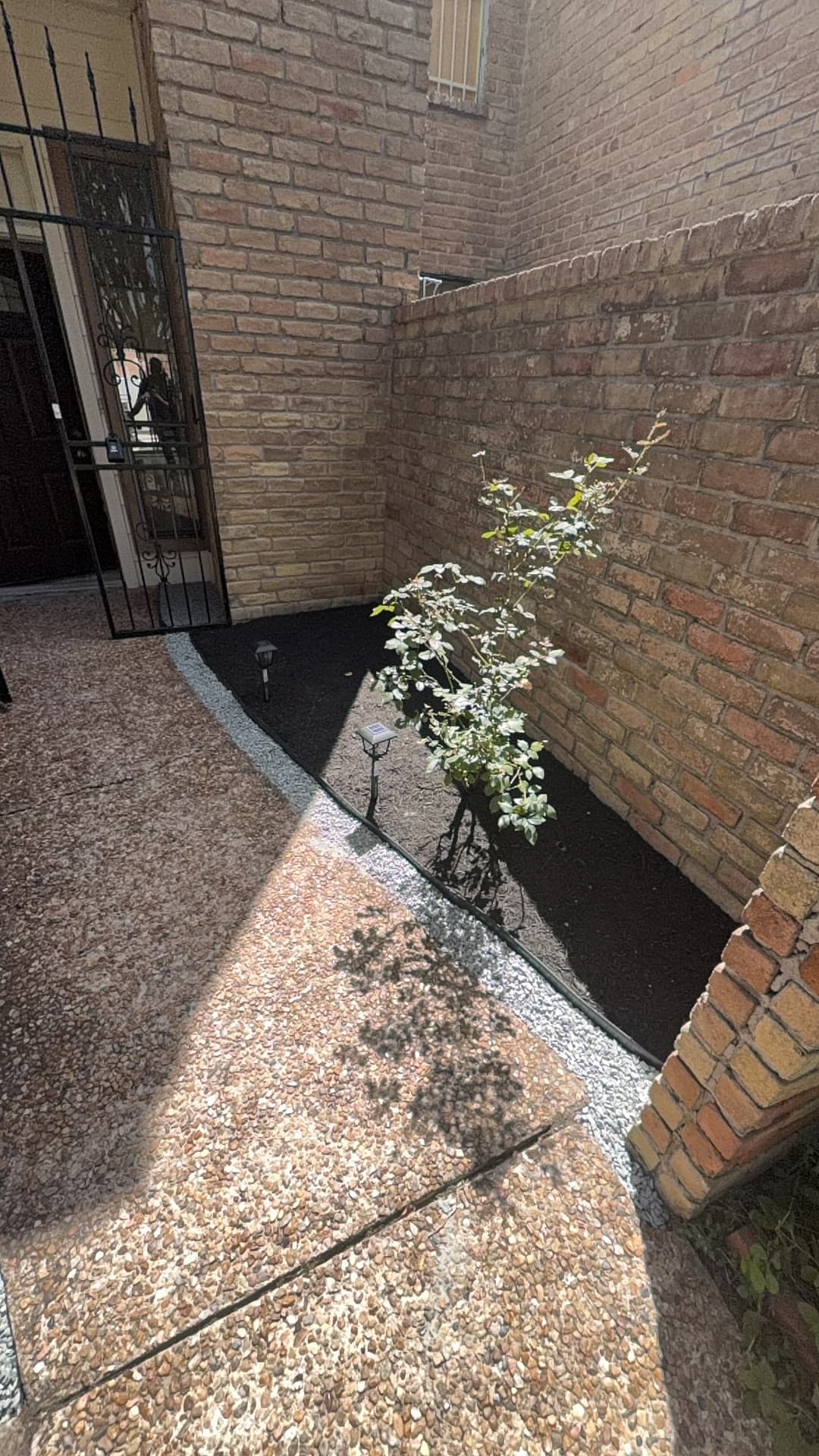 The same entry walkway cleared and re-laid with pea-gravel hardscape behind the iron gate