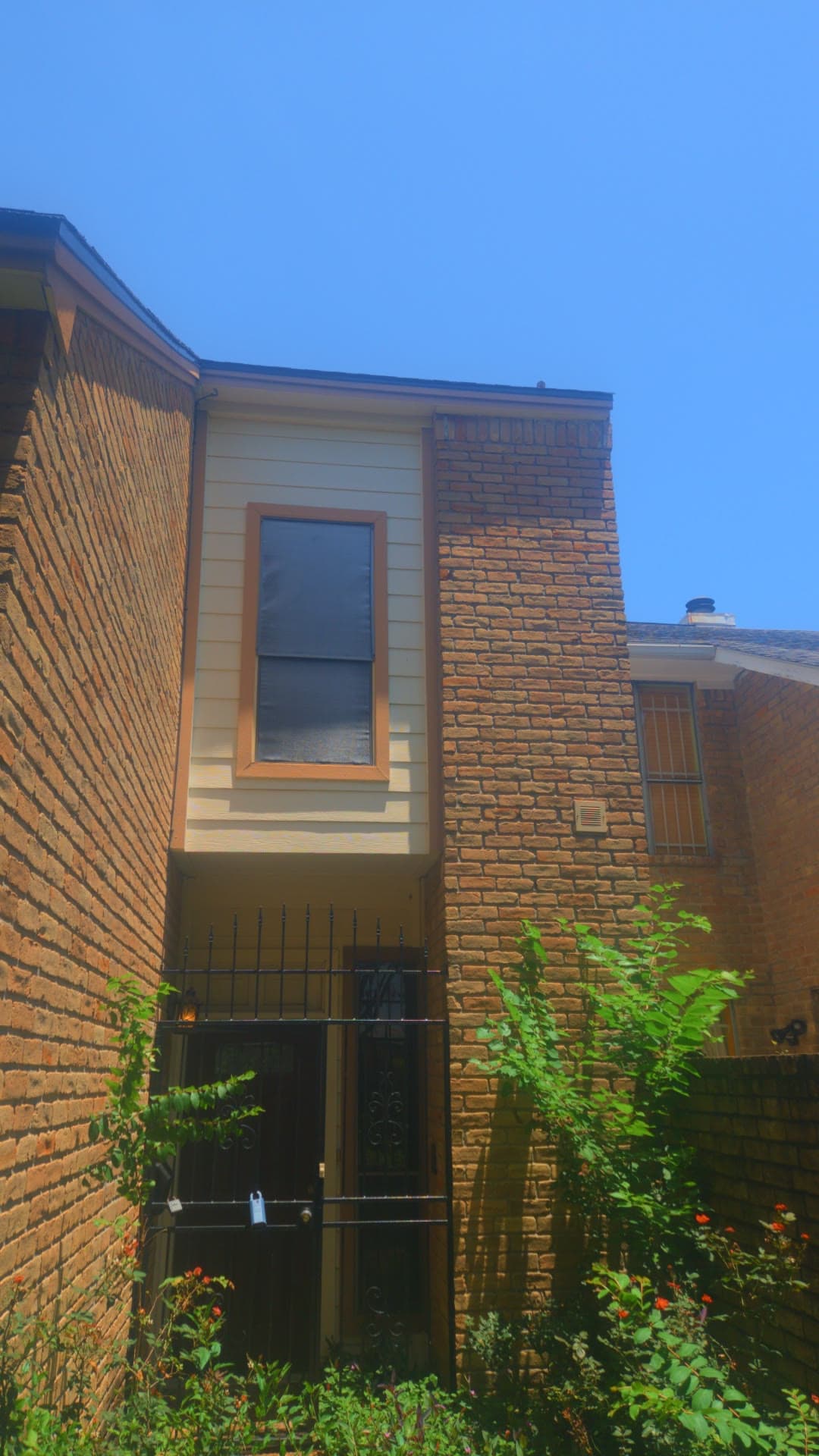 The brick facade and entry corner behind overgrown shrubs the day we took the keys