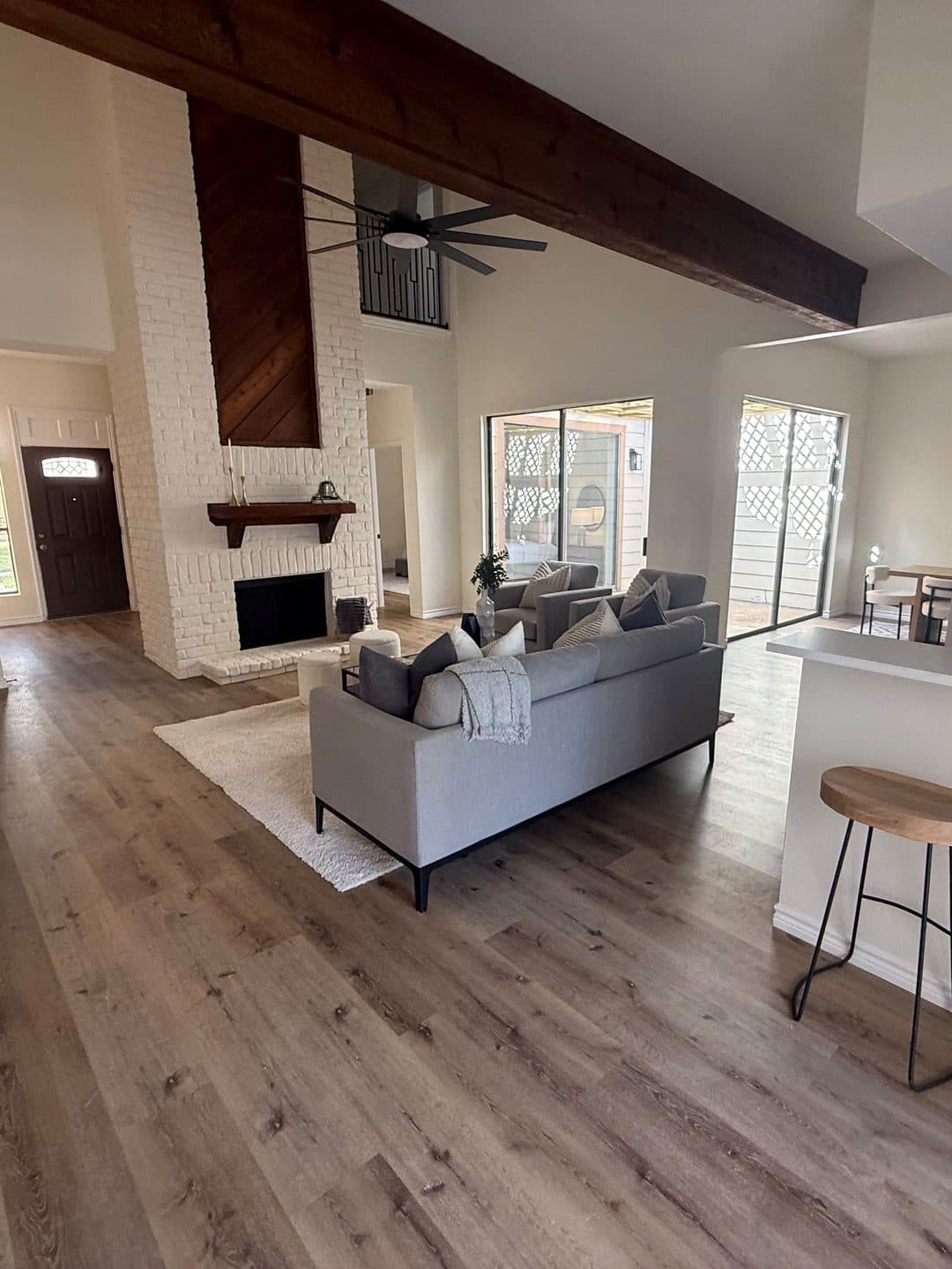 The same two-story fireplace finished and painted white, with the stained-wood chase kept, the beam exposed and the living room staged