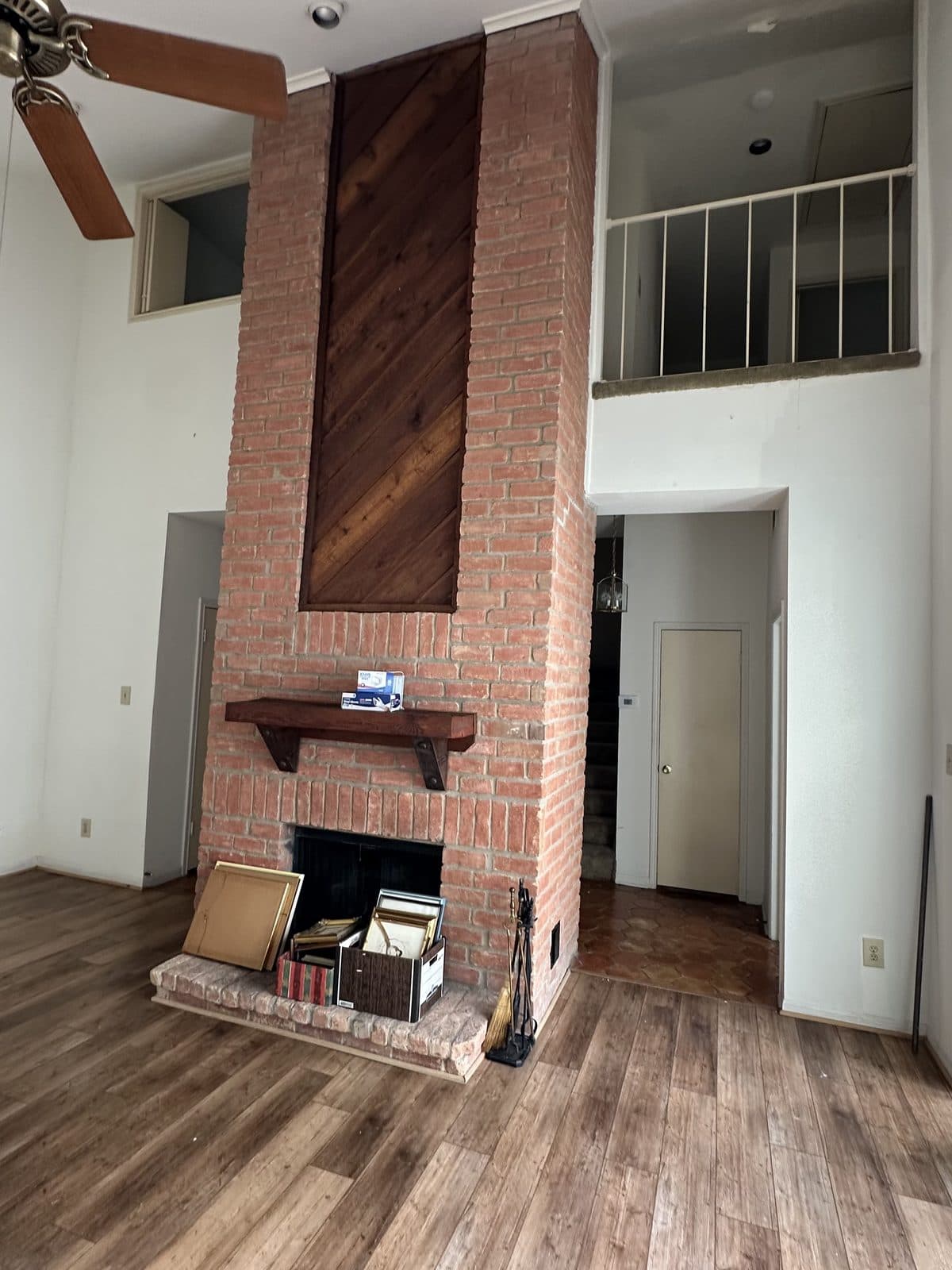 Two-story brick fireplace with a dark wood panel above the mantel, before demolition