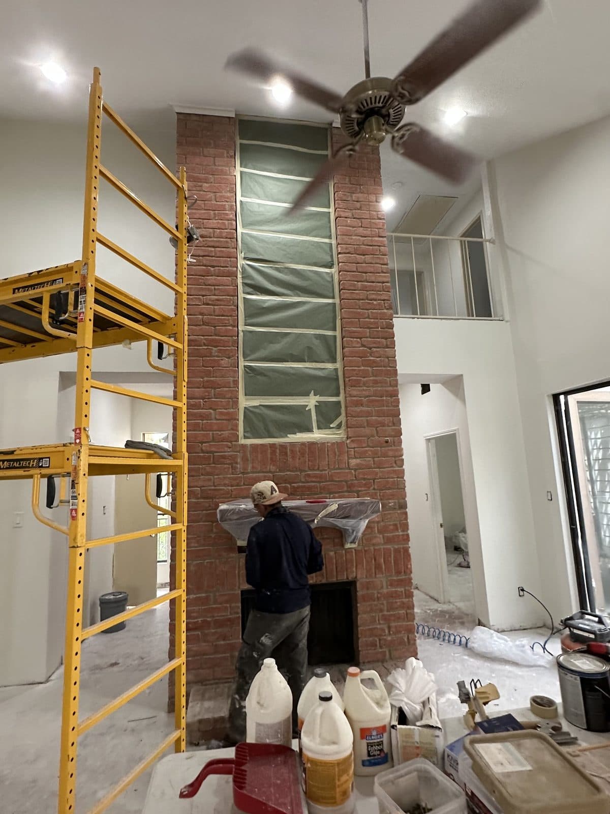 The same two-story fireplace with the chimney wrapped, scaffolding up and the walls painted