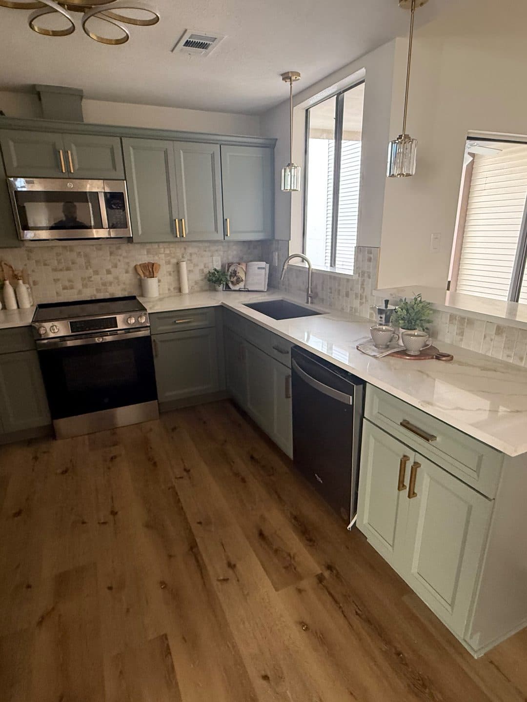 The same kitchen finished, with sage shaker cabinets, quartz counters, a stainless range and pendant lighting