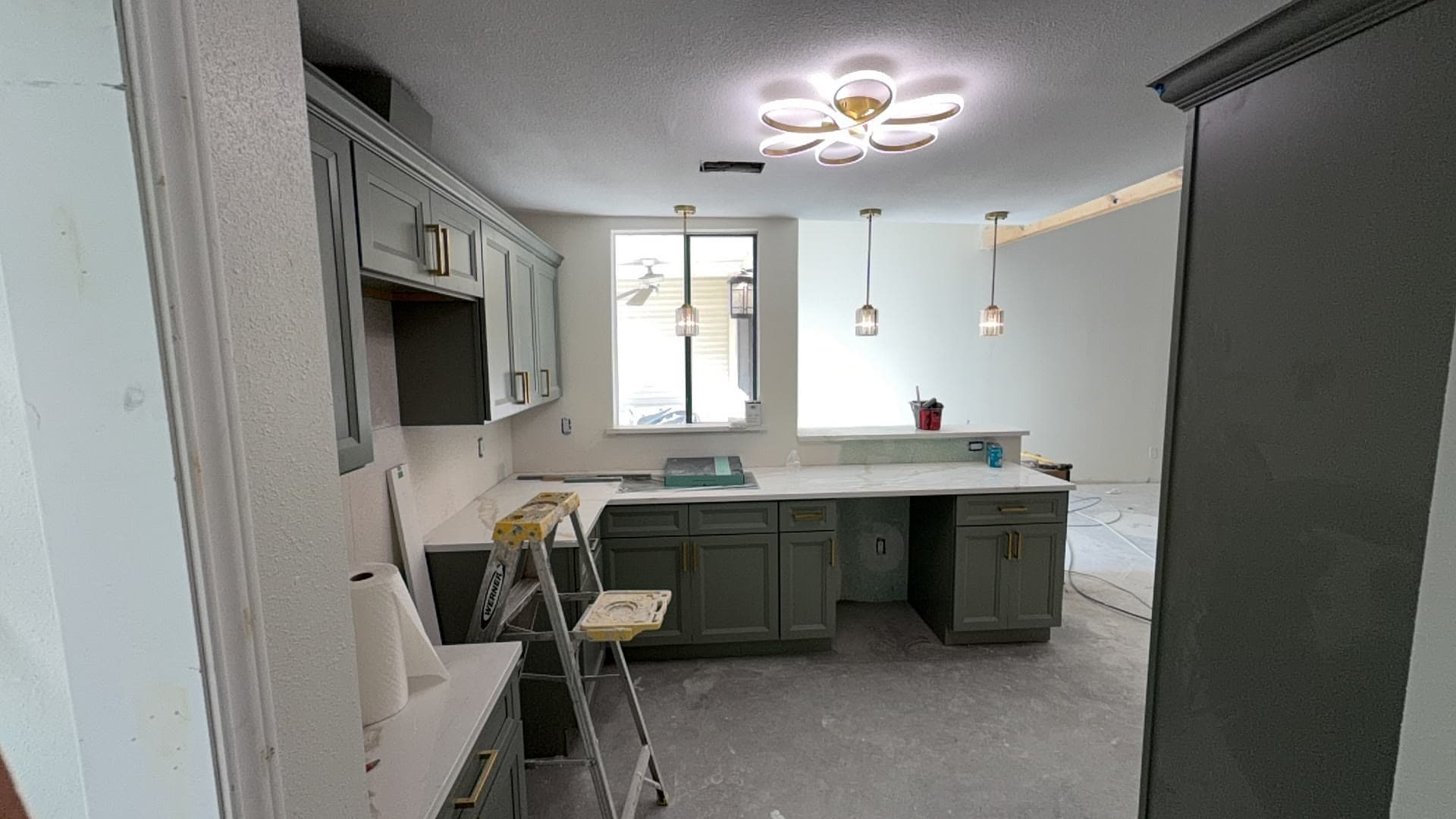 The renovated kitchen mid-build with new sage cabinets, quartz counters and pendant lighting
