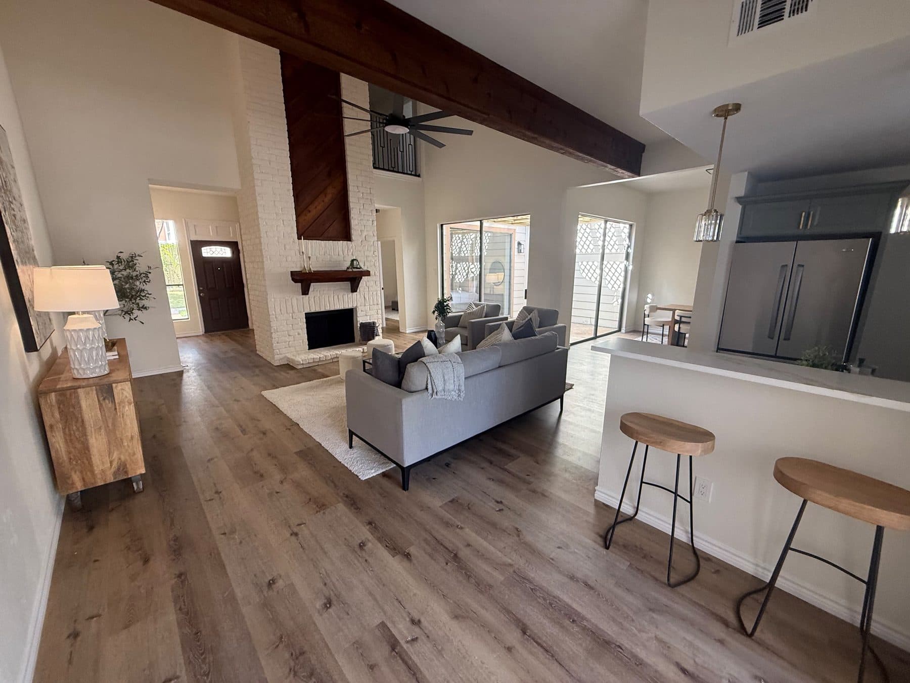 Living room with gray sectional, the white-painted two-story fireplace and the kitchen bar beyond, staged for listing and finished by the Reborn group