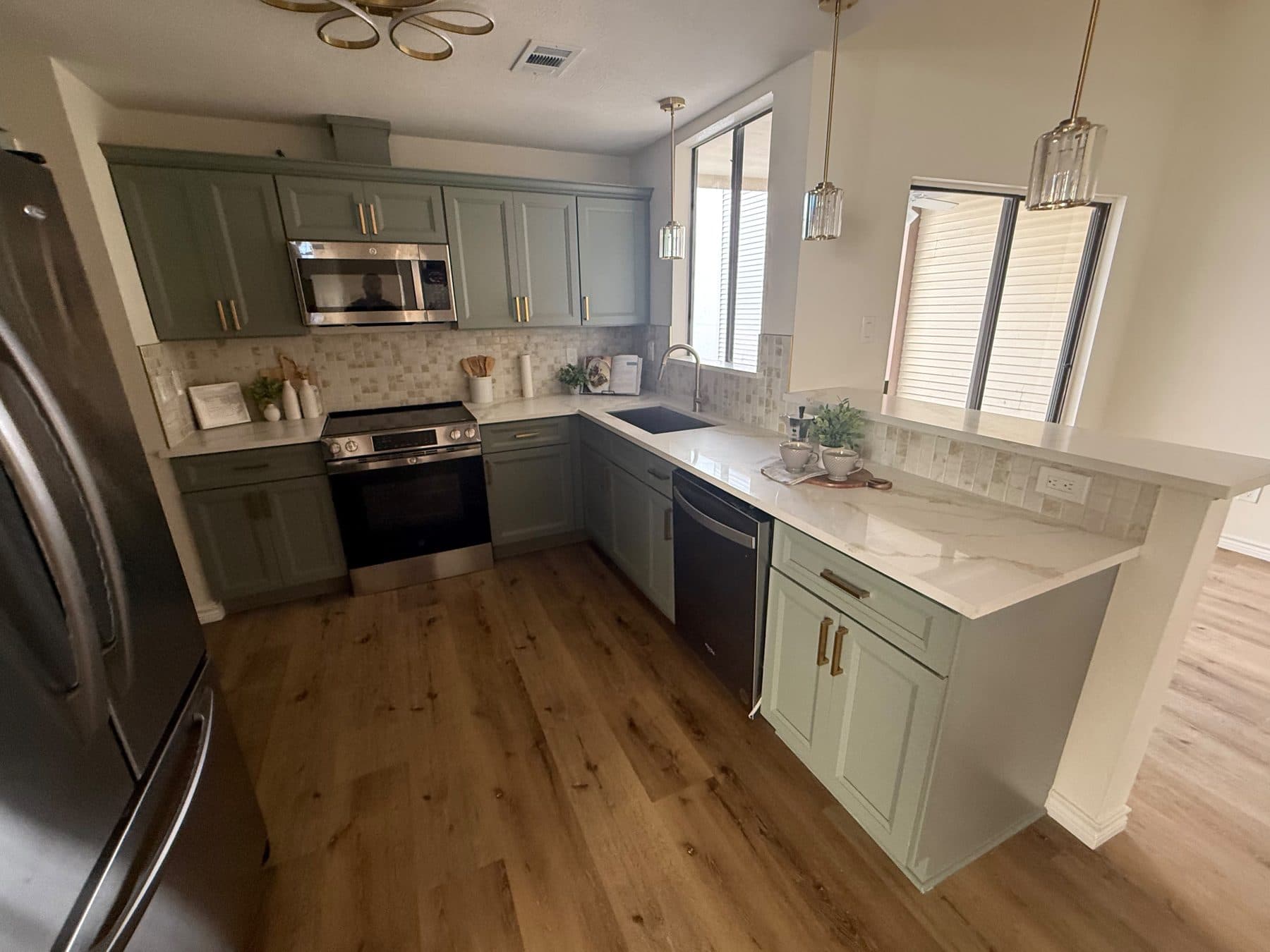 Kitchen with sage shaker cabinets, quartz counters, stainless range and pendant lights, finished by the Reborn group