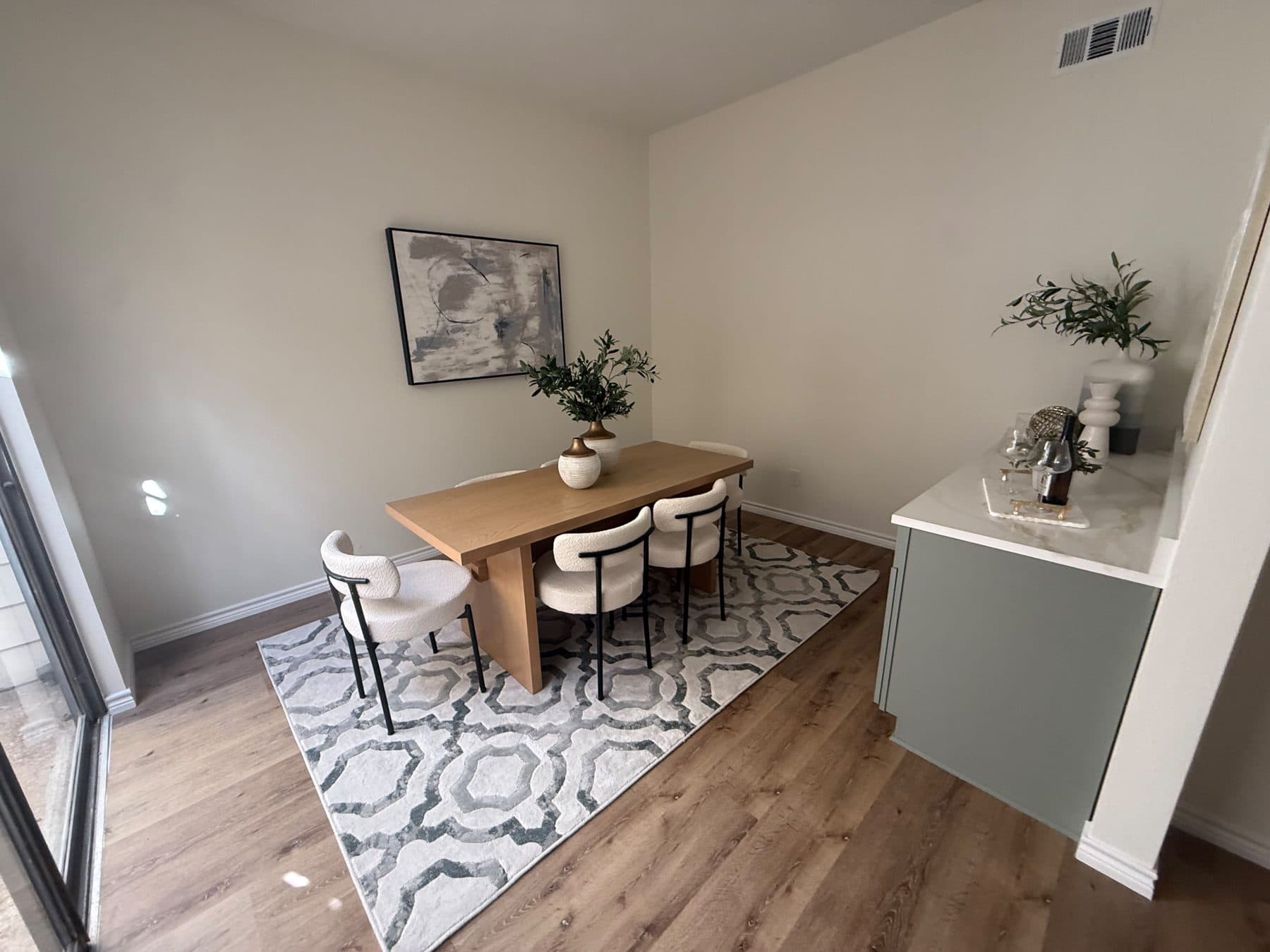 Dining room with a wood table, patterned rug and a sage sideboard, staged for listing and finished by the Reborn group