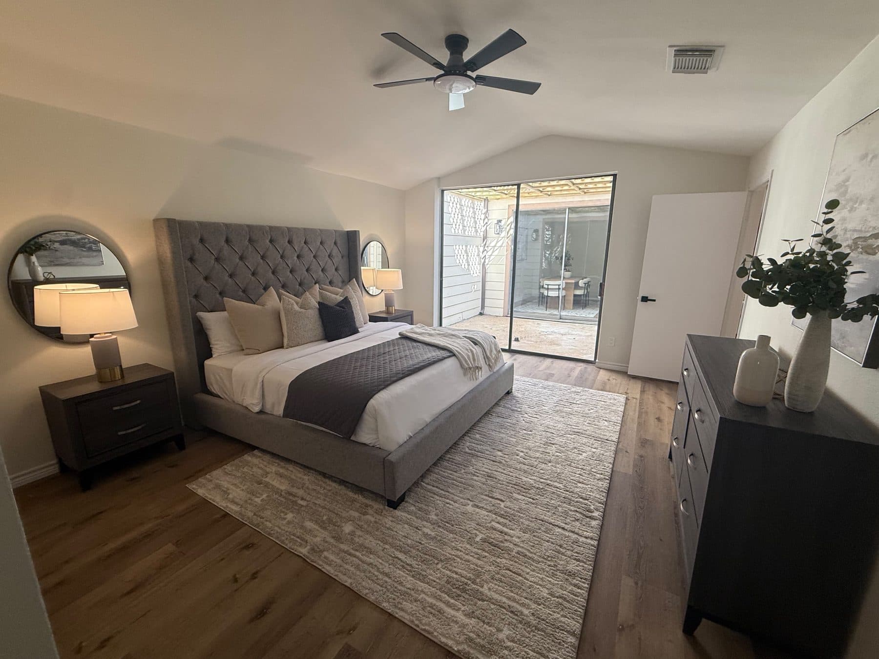 Primary bedroom with an upholstered gray bed and a slider to the patio, staged for listing and finished by the Reborn group