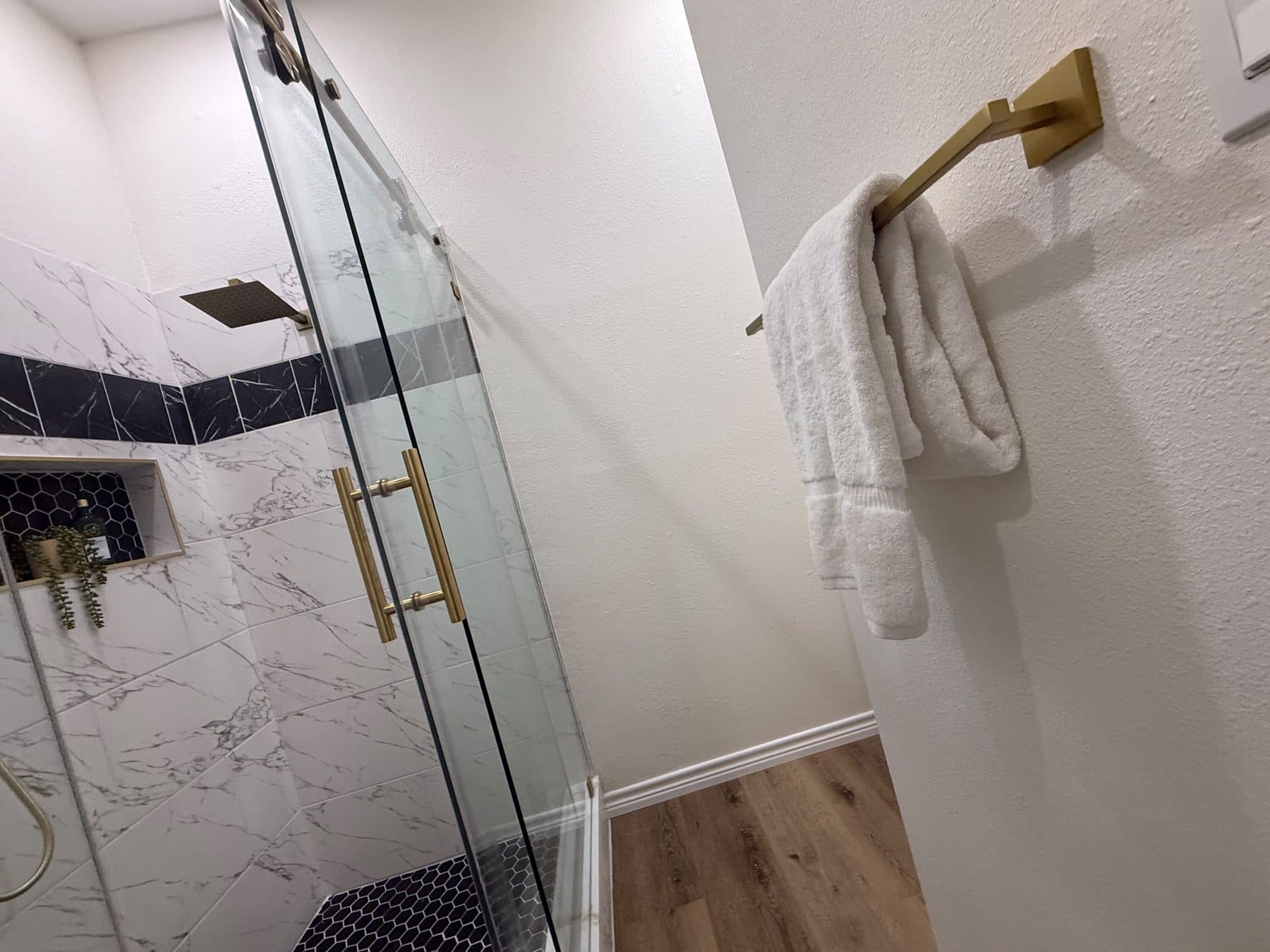 Primary shower with glass door, marble-look tile and brushed-gold hardware, finished by the Reborn group