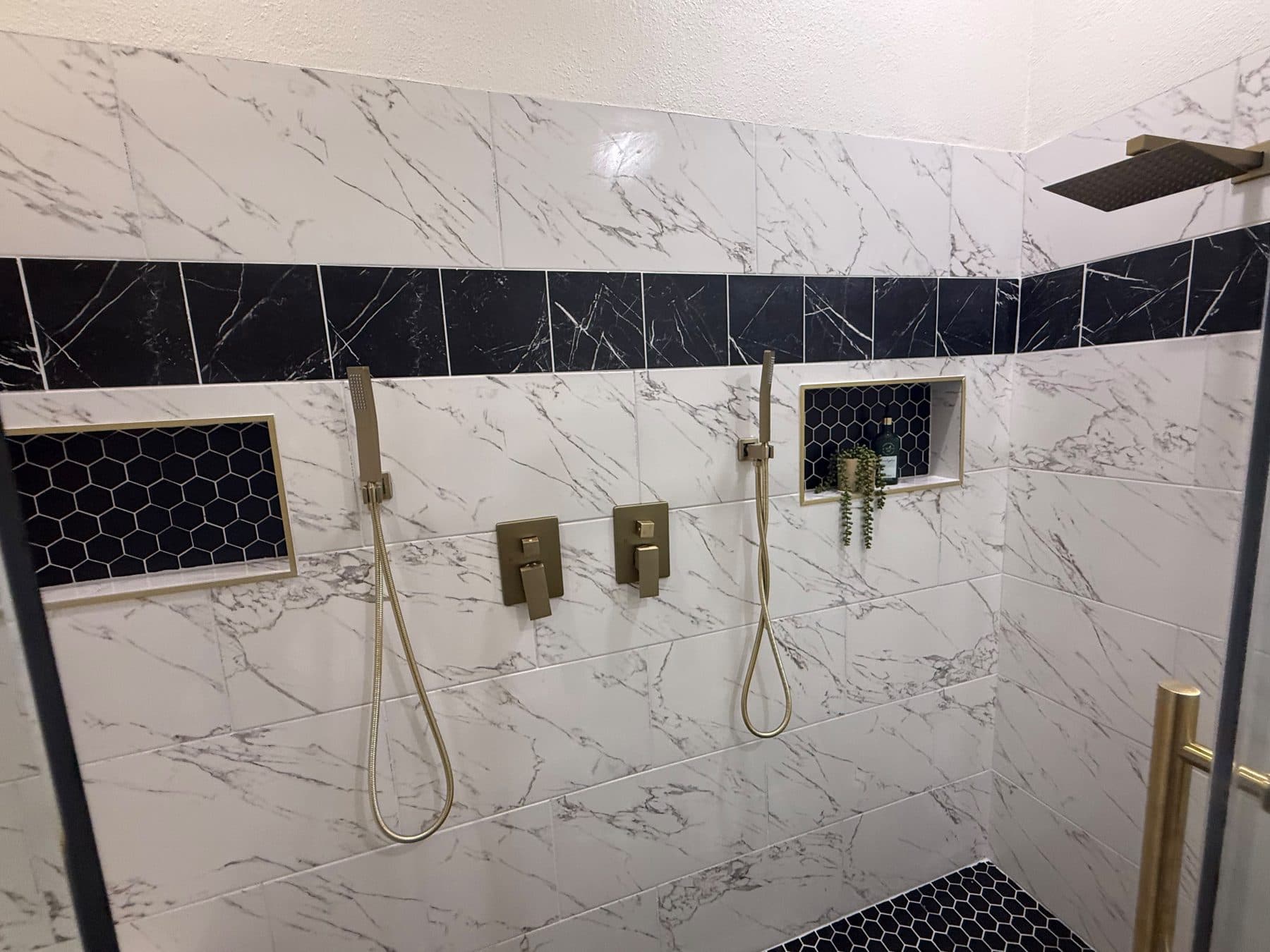Primary shower tile with a black accent band and gold fixtures, finished by the Reborn group
