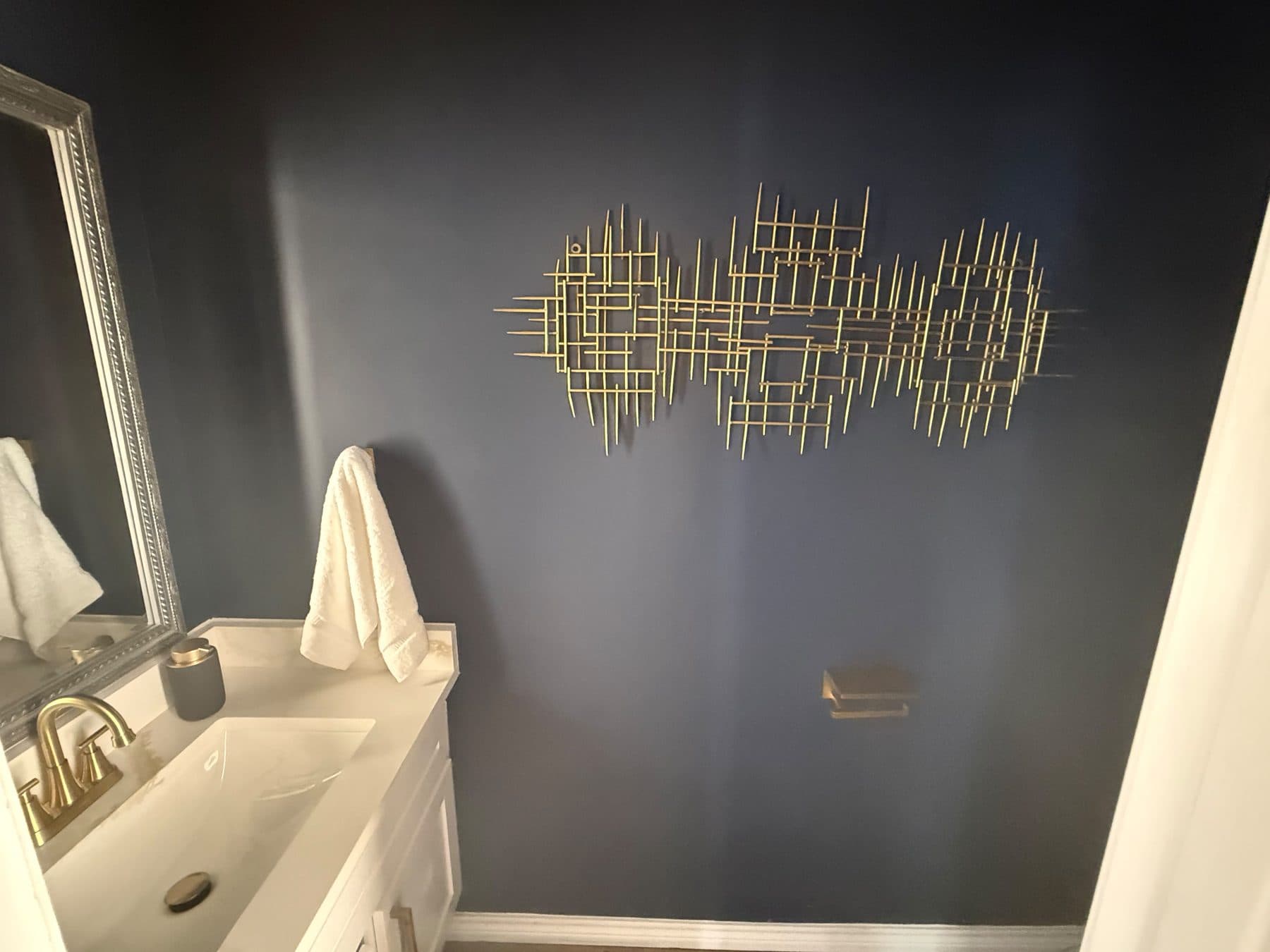 Navy powder room with gold wall art and a white vanity, staged for listing and finished by the Reborn group