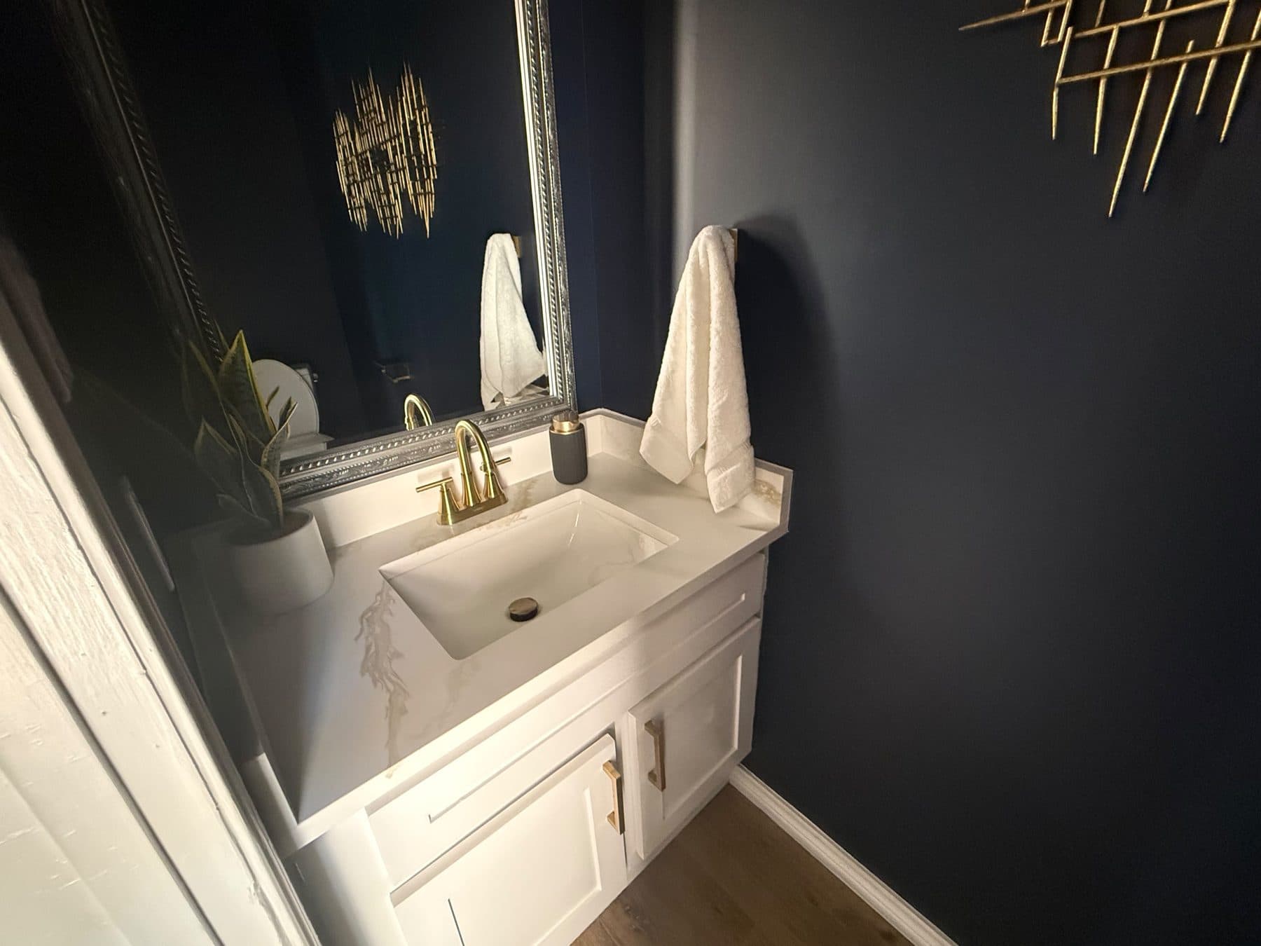 Powder room vanity with brushed-gold faucet and navy walls, finished by the Reborn group