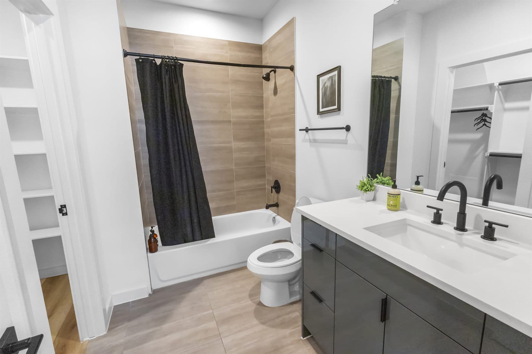 Tub and shower with black fixtures and wood-tone tile, finished by the Reborn group