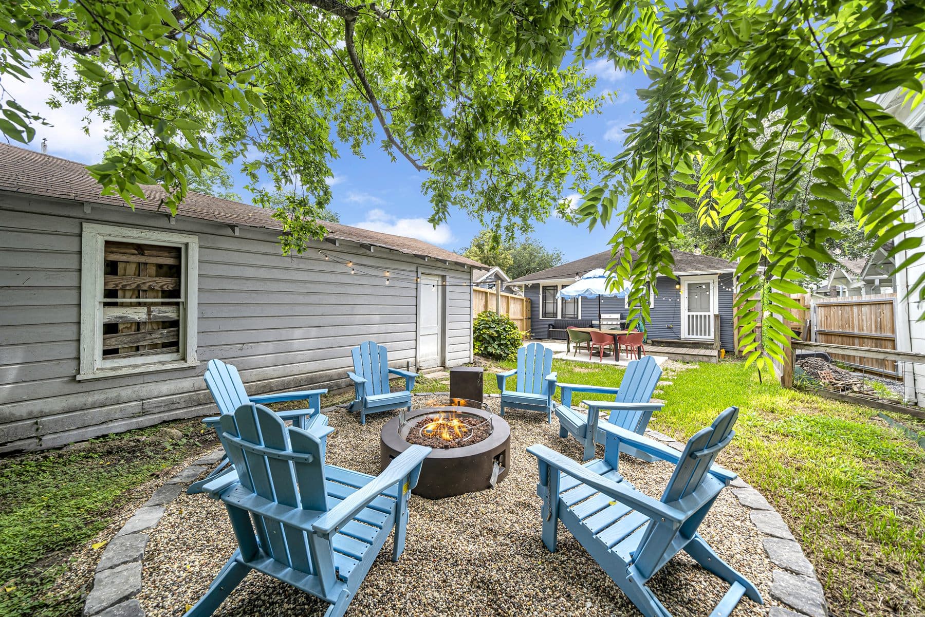 Adirondack chairs around a lit fire pit on a gravel patio with string lights, finished by the Reborn group