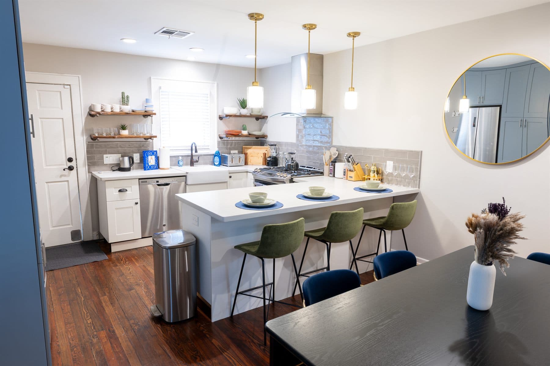 Kitchen island with pendant lights, gold barstools and floating shelves, finished by the Reborn group