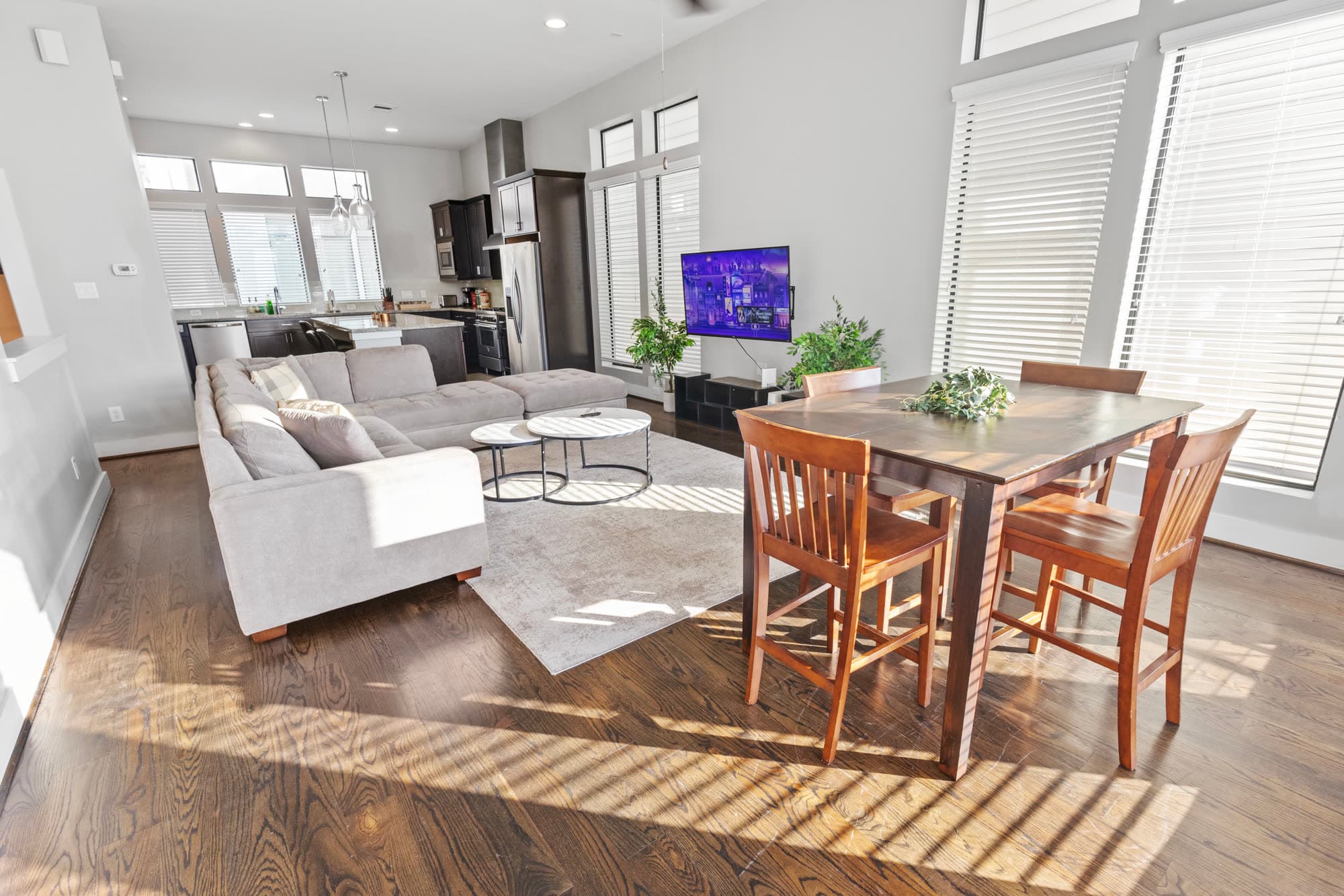 Light-filled living and dining room with a white sectional and wood dining table, furnished by the Reborn group