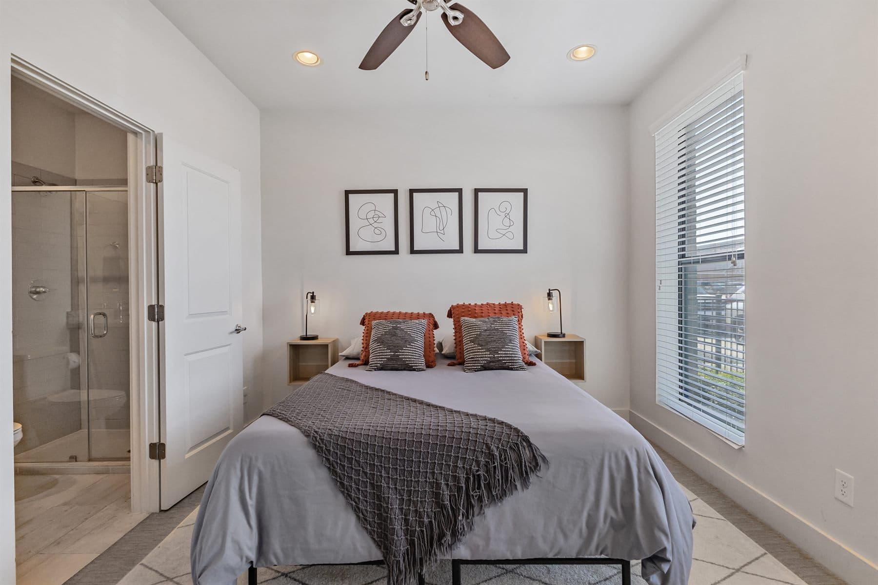 Neutral bedroom with rust bedspread, wood floors and framed art, finished by the Reborn group