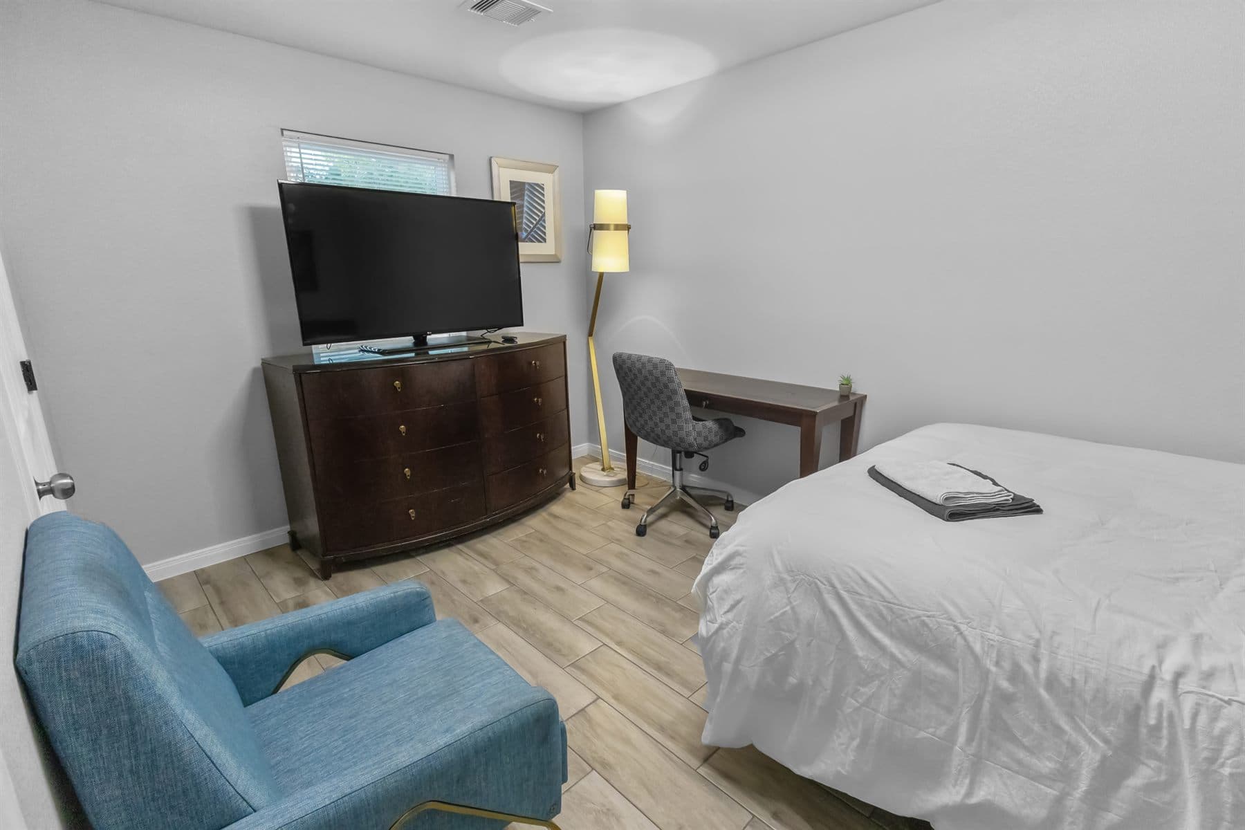Bedroom with desk, TV and teal accent chair, finished by the Reborn group